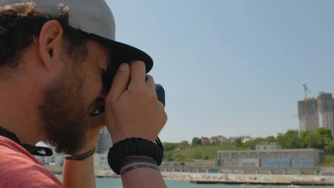 A man with a beard and in a cap makes a photo from the pier near the sea. 4 k Stock Footage 108325191