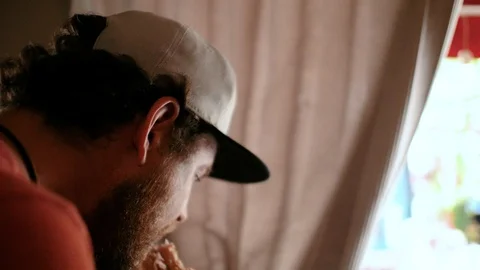 A man with a beard and a cap sits in a street cafe and bites a sandwich.4k video Stock Footage 109692125