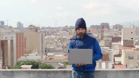 Man with a beard and cap working with a laptop in  a metropolis Stock Footage 139751777