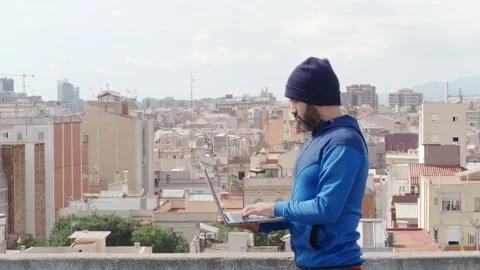 Man with a beard and cap working with a laptop with a metropolis Stock Footage 139751815