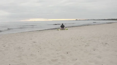 Man with Beard and Face Mask Meditating on Seashore at Dusk - Super Wide Dolly Stock Footage 130735169