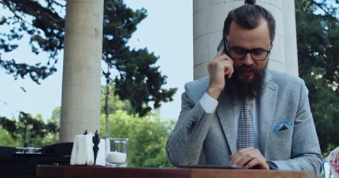 A man with a beard and glasses, dressed in business, speaks on the phone. Stock Footage 138930120