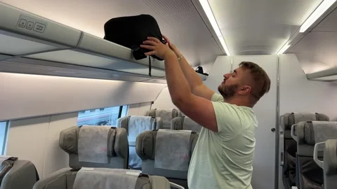Man with beard and green t-shirt puts black backpack on baggage rack Video stock 331172840