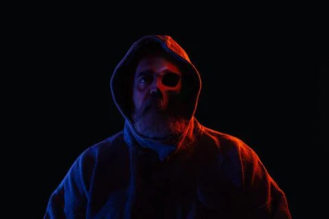 Man with beard and half face showing bones and skull in dark hoodie Stock Photos