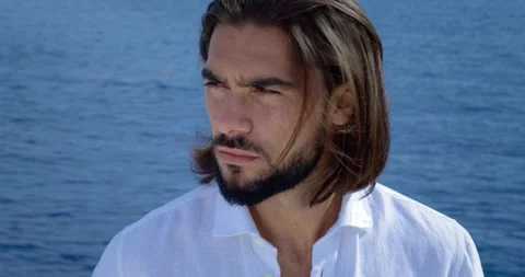 Man with a beard and long brown hair. We can see the blue sea in the background Video stock 154693715