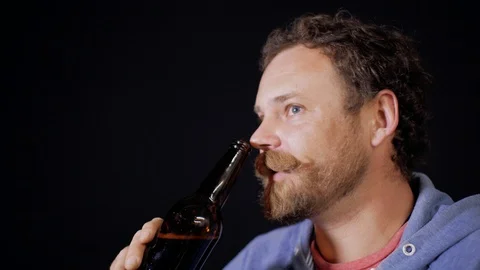 A man with a beard and mustache is drinking dark beer from a bottle Stock Footage 105840576