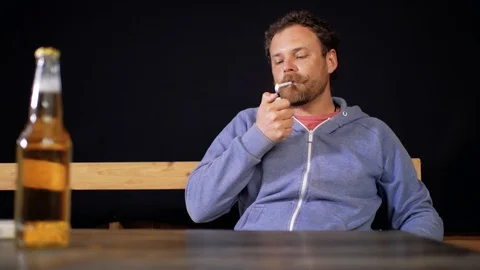 Man with a beard and mustache sits at the table lights a cigarette and smokes Stock Footage 105840693