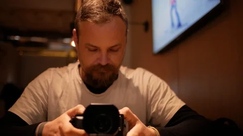 A man with a beard and mustache is sitting in a cafe at the table and holding Stock Footage 99779089