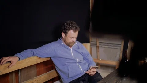 A man with a beard and mustache is sitting at the table writing sms on his phone Stock Footage 105840659