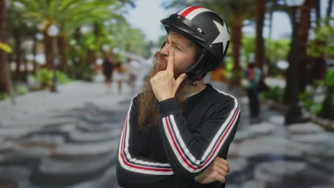 Man with beard and star patterned helmet resting hand on chin in green park.. Stock Footage 314627184