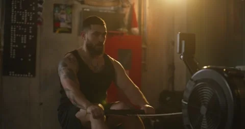 Man with beard and tattoo doing rowing exercises on machine during his strength Stock Footage 313422275