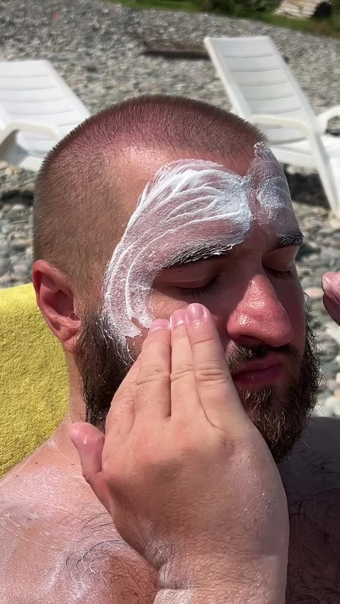 Man with beard applies moisturizer to face on sun lounger on sea beach Video stock 331172962