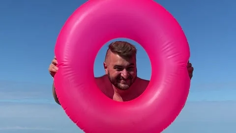 Man with beard, big belly looks out from pink swim ring Stock-Footage 332560853