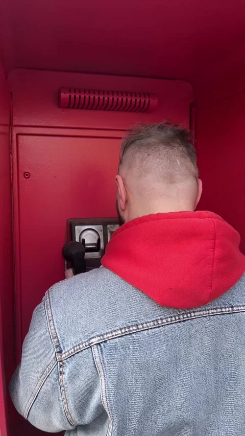 Man with beard in blue denim jacket in red telephone booth calling on payphone Stock Footage 303083867