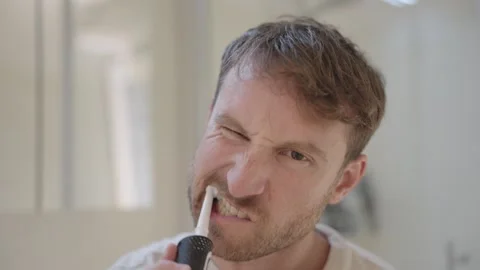 Man with a beard brushing his teeth with an electric toothbrush during his Stock Footage 335196921