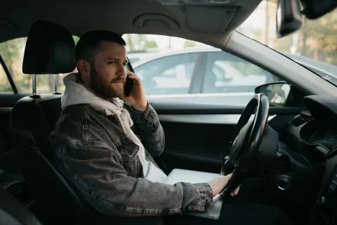 A man with a beard in casual clothes doing calls on his smartphone inside a c Stock Photos