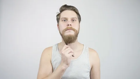 A man with a beard combs beard looking at myself in the mirror. 動画素材 121688316