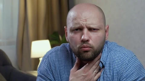 A man with a beard coughs very hard looking at the camera. Choked Stock Footage 242599691