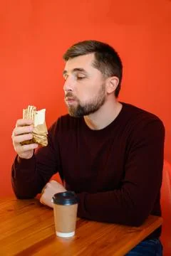 A man with a beard eats shawarma, a quick, tasty and healthy snack at a fas.. Stock Photos