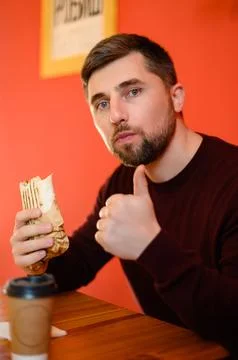 A man with a beard eats shawarma, a quick, tasty and healthy snack at a fas.. Stock Photos