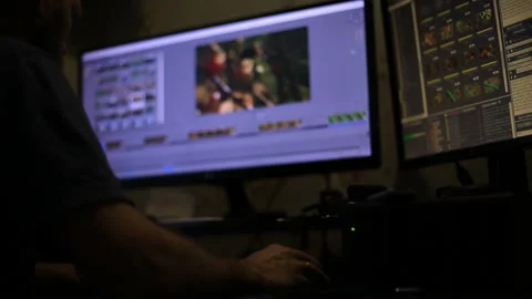 A man with a beard editing video in the program, sitting at two monitors and dri Video stock 98535634