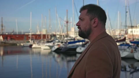 A man with a beard in an elegant coat close-up walks along the promenade with Stock Footage 221804457