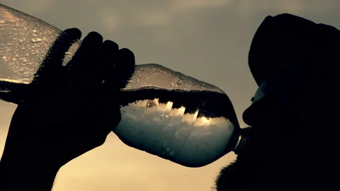 A man with a beard in glasses and a cap drinks water from a bottle at sunset. Stock Footage 147049133