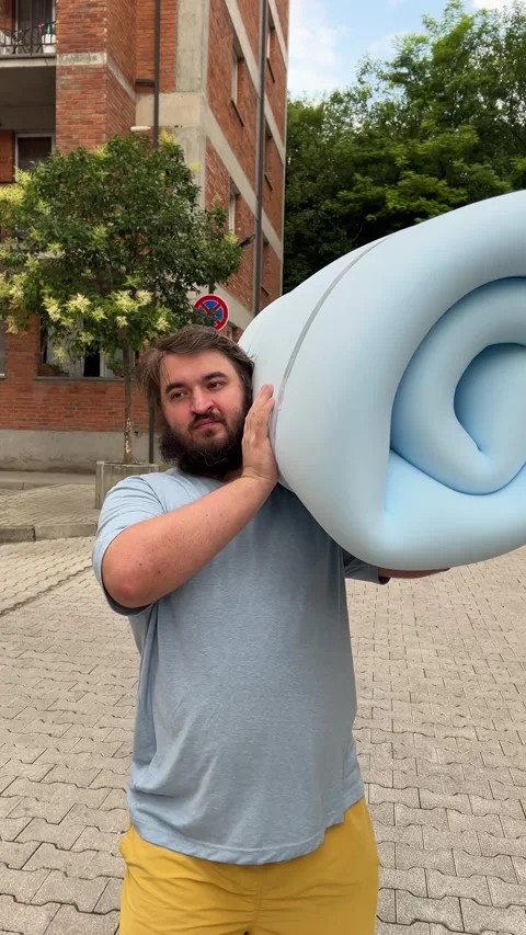 Man with beard holds blue bundle of foam rubber, walks in yard Video stock 340427577