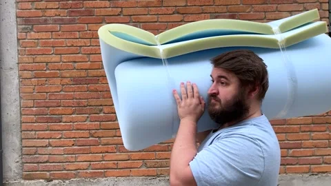 Man with beard holds blue bundle of foam rubber, walks near brick wall Stock Footage 340428028