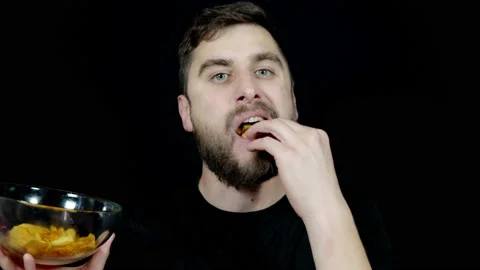 A man with a beard holds a bowl of chips in his hands and eats Stock Footage 139640497