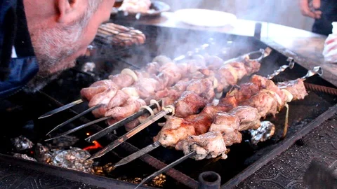 A man with a beard inflates coal under meat roasting on a fire Stockbeeldmateriaal 105426293