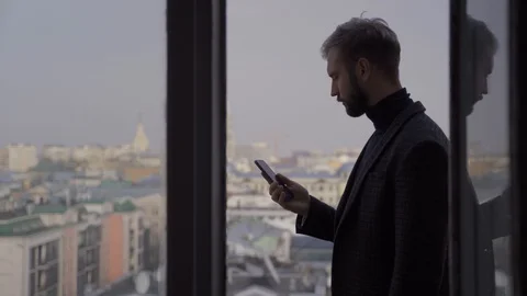 A man with a beard in a jacket talks on the phone on the balcony of a tall build Stock Footage 128360518