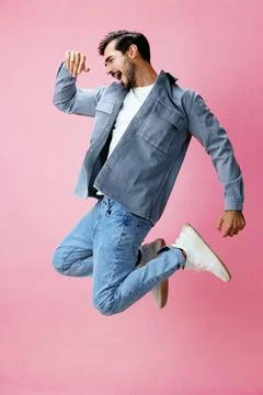 Man with beard jumping on pink background in white T-shirt and jeans, smile and Stock Photos