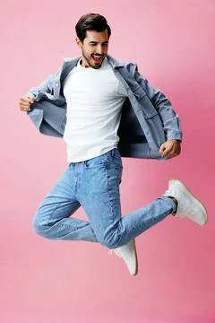 Man with beard jumping on pink background in white T-shirt and jeans, smile and Stock Photos