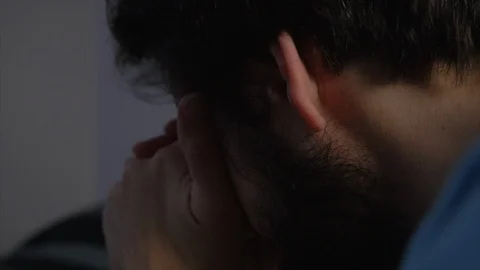 A man with a beard kneeling by his bed with hands on his face, whilst Stock Footage 100334753
