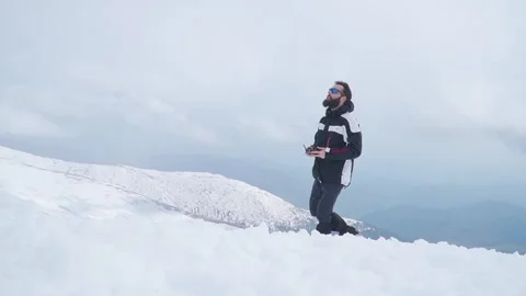 Man with beard launches drone from hand while standing in snow high on Stock Footage 249048091