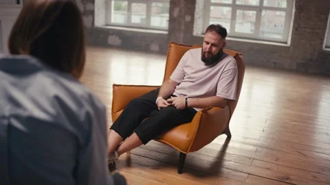 A man with a beard in a light pink brown chair talks about his problem to a Stock Footage 252251544