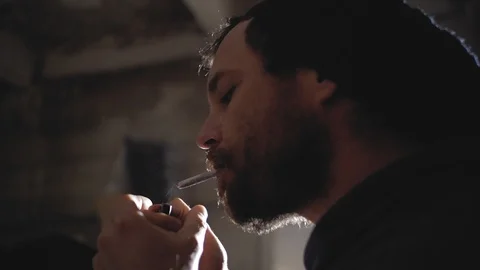A man with a beard lights up and smokes, releasing smoke.marijuana smoking Видео 102942237