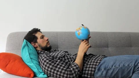 Man with beard lying on a couch watching and spinning a small world globle Video stock 340583420