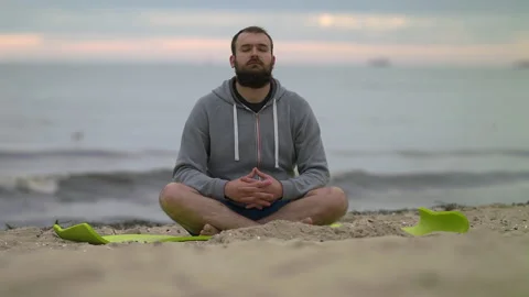 Man with Beard Meditating on Seashore at Dusk - Wide Shot Stock Footage 130732656