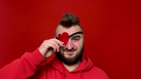 Man with beard, mohawk, heart shaped occluder in red hoodie looks at camera Video stock 300399062