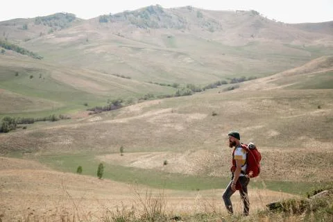 Man with beard mustache with a backpack goes mountains summer looks around. Stock Photos