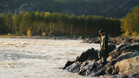 Man beard mustache raincoat is standing near a river with a bucket Stock Footage 111499802