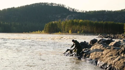 Man beard mustache raincoat is standing near a river with a bucket Stock Footage 111499846