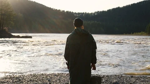 Man beard mustache raincoat is standing near a river with a bucket Stock Footage 111499861