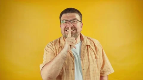 Man with beard on orange background holding index finger in front of mouth Stock Footage 158157335