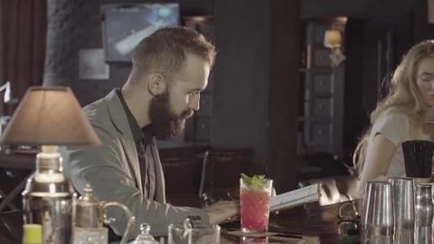 A man with a beard orders a drink in a bar for himself and an attractive blonde Stock Footage 76949686