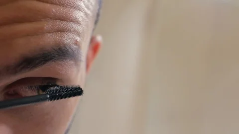 A man with a beard paints eyelashes with mascara. Pretty man applying makeup.4k Stock Footage 111801363