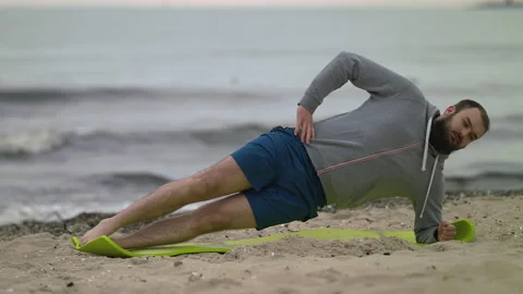 Man with Beard Performing Side Elbow Plank on Seashore at Dusk - Wide Shot Stock Footage 130729139