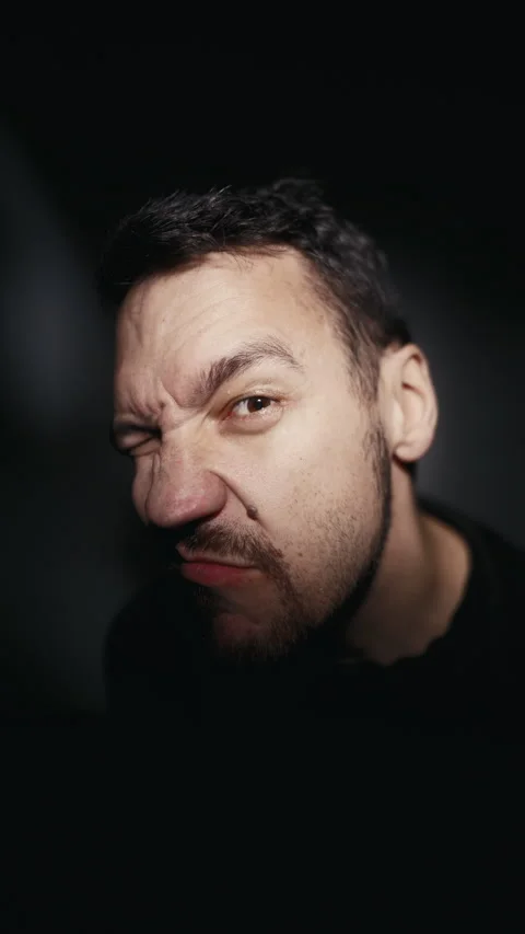 A man with a beard is playfully contorting his facial features in dim lighting Stock Footage 270924237